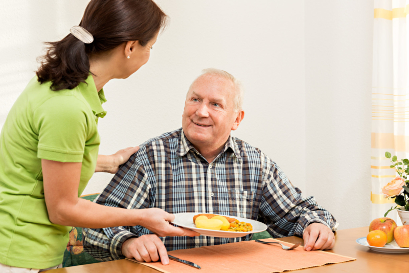 Caregiver giving senior man lunch in the kitchen