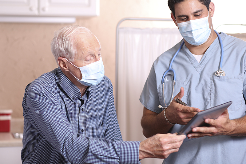 masked senior man talking with healthcare professional