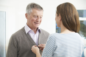 Adult Daughter Helping Senior Man To Button Cardigan