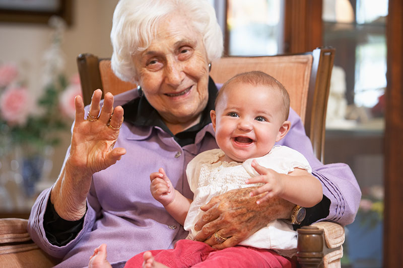 An older woman holds a smiling baby on her lap