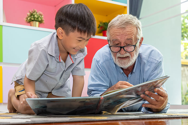 An older man reads a book to his grandson