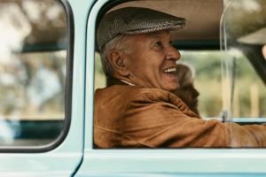 An older gentleman is smiling and riding in a vintage vehicle, participating in a creative dementia therapy technique called reminiscence therapy.