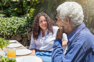 A woman sits with an older man at a dining table outdoors, trying to figure out what to expect in dementia.