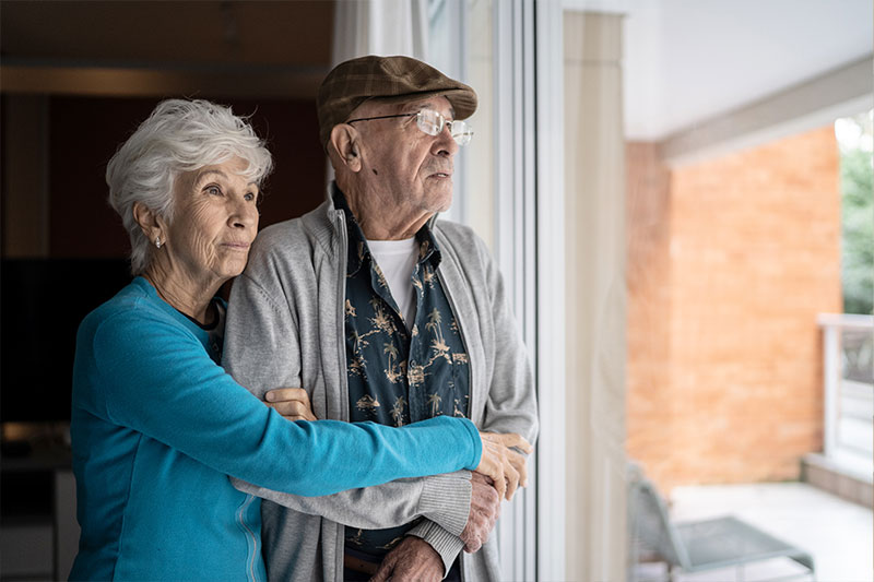 A woman who knows that providing care for your spouse can cause resentment hugs her husband as they both look out the window.