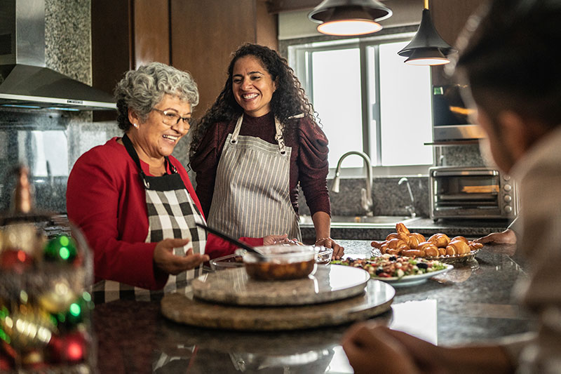 A woman who knows how to relieve holiday stress for caregivers smiles and helps her elderly mother prepare holiday treats.