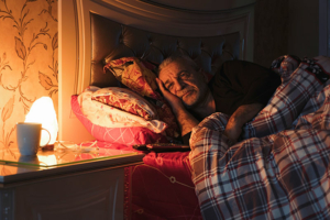 A man lies awake in bed. It can be difficult for family members to know how to help a senior loved one sleep better.