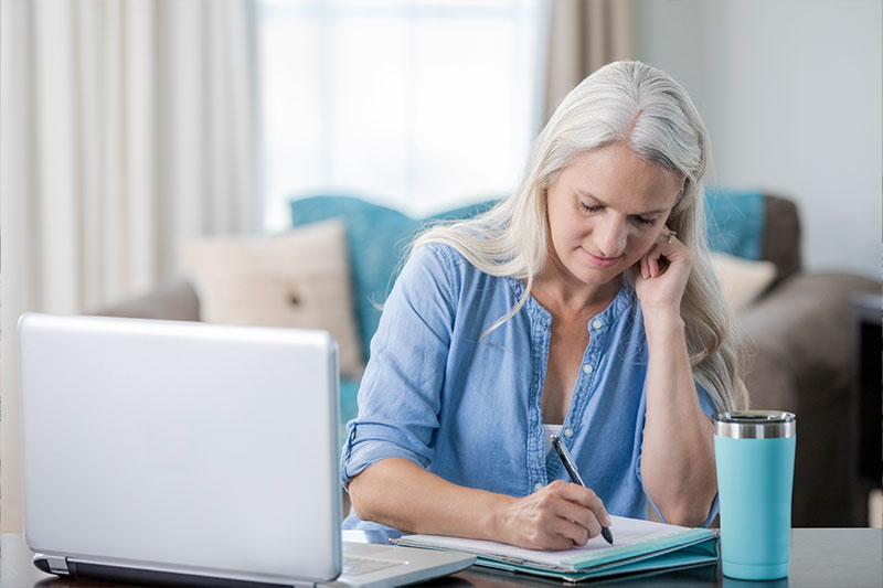 A woman who has learned how to reduce family caregiver stress smiles as she writes a note in her daily planner.