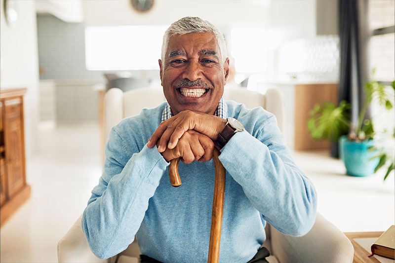 An older man who has overcome his fear of falling smiles confidently as he leans on his cane.