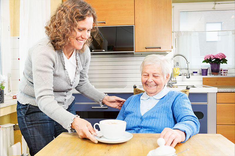 An older woman receiving respite care services in Fort Lauderdale smiles as her caregiver serves her a cup of coffee.