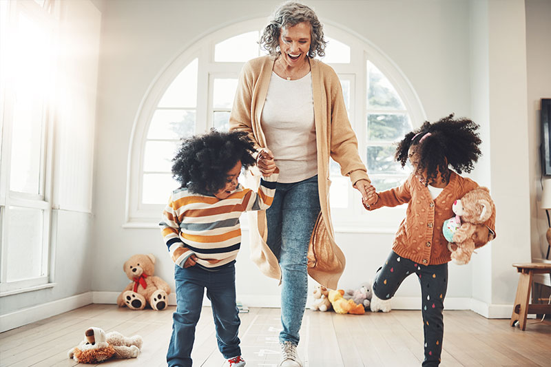 A woman who knows the importance of improving your balance holds the hands of her grandchildren as they exercise.