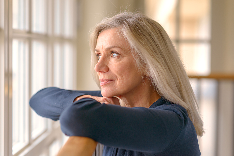 A woman looks out a window, practicing strategies for coping with caregiver frustration as she cares for her mother who has dementia.