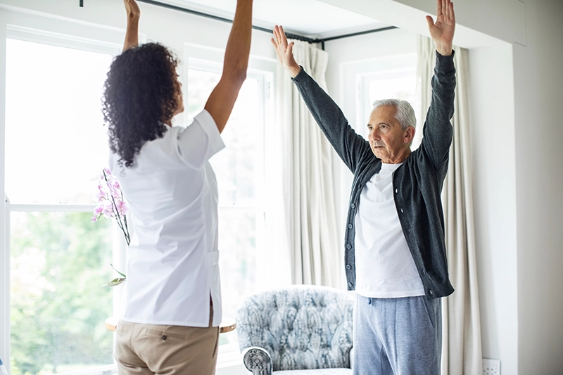 A caregiver guides an older adult through mind-body exercise for seniors to improve balance and flexibility.